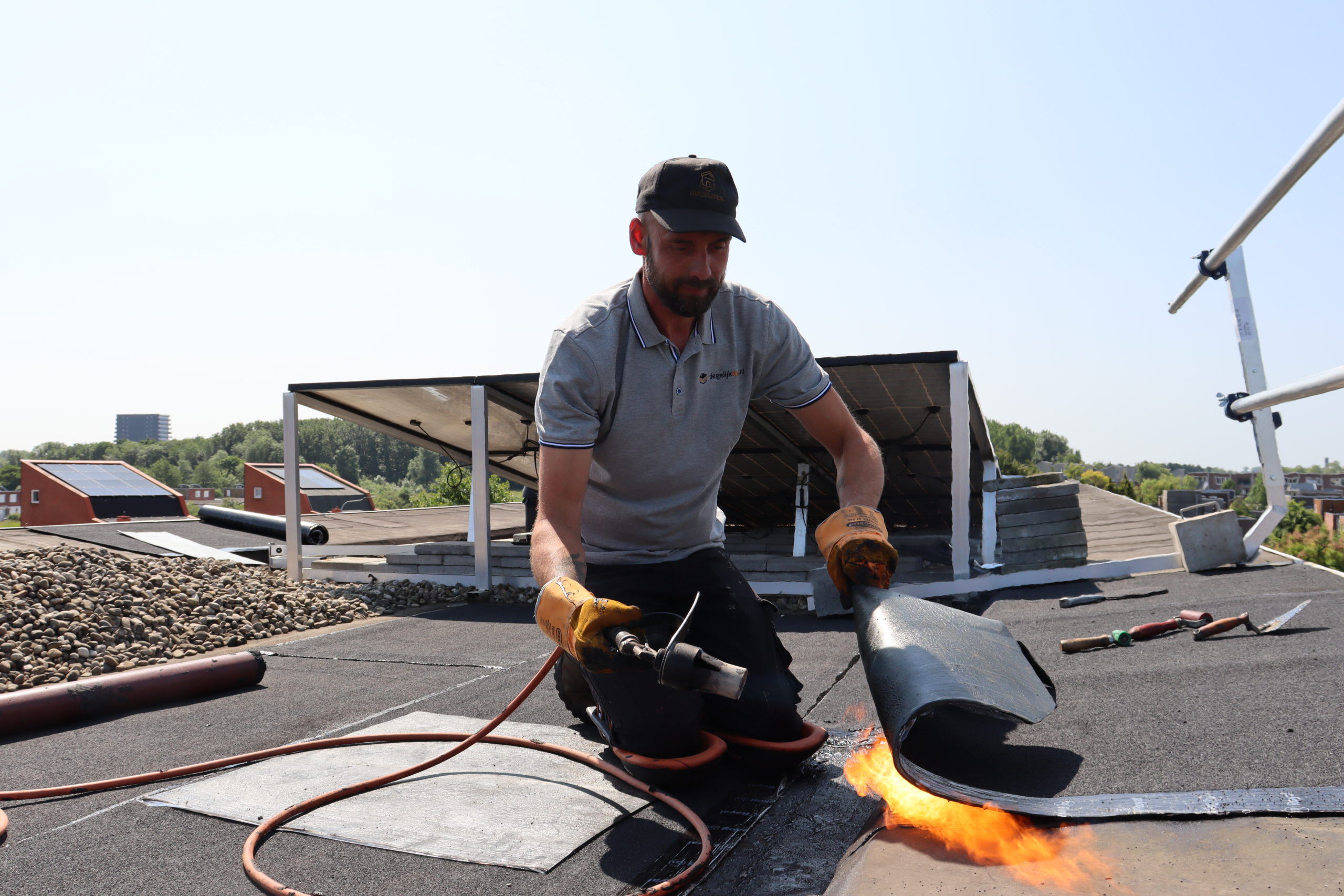 Dakdekker van Degelijkdak brandt bitumen dakbedekking vast op plat dak met gasbrander.